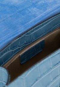 Sac à main en cuir de crocodile bleu avec rabat en daim, montrant une poche intérieure zippée et un revêtement en tissu marron.