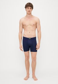 Μπλέ σεντόνια boxer με εφαρμοστό σχέδιο, ελαστική μέση και λεία υφή; φορεμένα από μοντέλο που στέκεται ξυπόλητο και χωρίς μπλούζα.