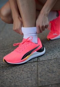 Zapatillas deportivas de color rosa brillante con un upper de tela texturizada, franja de acento negra, suela blanca y detalle del talón amarillo en contraste.