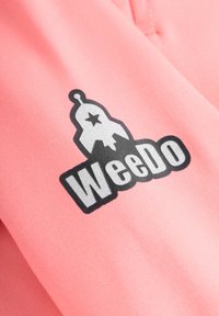 Lichtroze stof met een zwarte grafische print van een raket en de tekst "WeeDo" in vetgedrukte letters. De textuur lijkt glad en schoon.