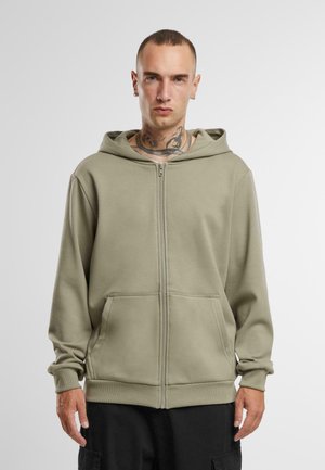 Sweat à capuche zippé vert olive en tissu doux, avec une grande capuche, des poches avant, des manches longues et des poignets et un ourlet côtelés.