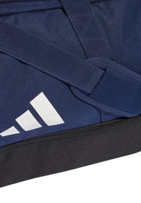 Námornícky modrý dufflový vak s čiernym dnom, s bielym logom Adidas, pevným popruhom a textúrovanou tkaninou pre trvanlivosť.