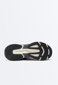 Schwarze und beige Gummisohle eines Sportschuhs mit Profilmustern und der Markenbezeichnung „Oysho“ in der Mitte.