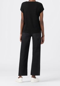 Svart t-shirt med korta ärmar, i kombination med vida svarta jeans och vita sneakers. Tyget ser mjukt ut med en avslappnad passform och minimala detaljer.