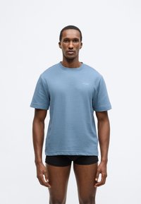 Világoskék, texturált, rövid ujjú póló kerek nyakkivágással, a bal mellkason egy kis fehér logóval.