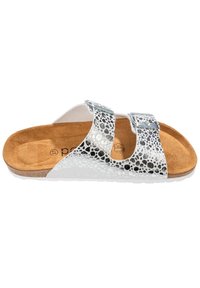 Sandal med två justerbara silverfärgade spännen som har ett svart och vitt prickigt mönster och en beige formad fotbädd.