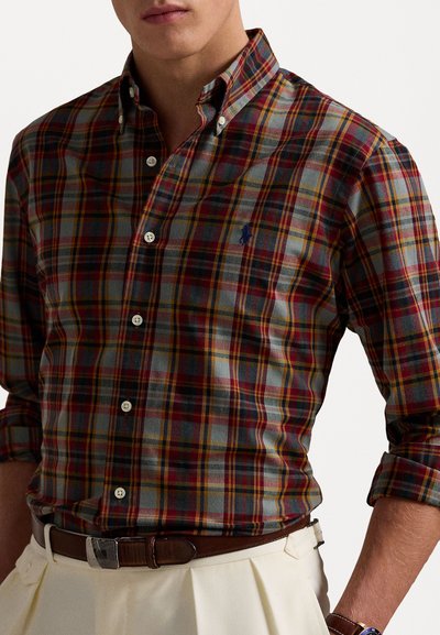 Chemise à carreaux dans des teintes de rouge, bleu et jaune, avec un col boutonné, des manches longues et des boutons blancs. Présente un petit logo sur la poitrine.