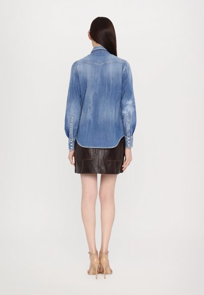 Denim shirt with a slightly faded blue wash, long sleeves, and button cuffs, paired with a brown leather mini skirt featuring front pockets.
