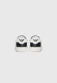 Baskets noir et blanc avec une tige en cuir lisse, une semelle en caoutchouc et un logo distinctif sur le talon. Design minimaliste.