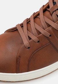Brązowe skórzane sneakersy z dopasowanymi brązowymi sznurowadłami i białą gumową podeszwą, ukazujące szczegółowe szwy oraz teksturowaną skórzaną powierzchnię.