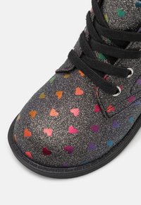 Glitzernder schwarzer Knöchelstiefel mit mehrfarbigen Herzmustern, schwarzen Schnürsenkeln und silbernen Ösen; runde Zehenpartie und strukturierte Oberfläche.