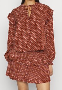 Rote gemusterte Bluse mit Rüschensleeven und gebundenem Ausschnitt, kombiniert mit einem passenden, stufenförmigen, gerafften Rock im gleichen Stoffdesign.