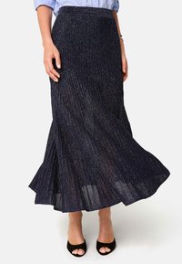 Marineblaue plissierte Midi-Rock mit metallic Faden, aus strukturierter Stoff, mit einem ausgestellten Saum, kombiniert mit schwarzen, offenen Absatzschuhen.