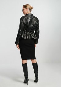 Czarna skórzana kurtka z marszczeniem w talii, zestawiona z teksturowaną czarną spódnicą i wysokimi na kolano czarnymi szpilkami. Gładkie, błyszczące wykończenie.