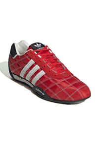 Röd idrottssko med ett kviltat mönster, med tre vita ränder, en svart häl och tunga, samt röda snören. Gummisula för grepp.