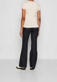 Top de manga corta rosa claro combinado con jeans acampanados azul oscuro. Los jeans cuentan con costuras sutiles y un diseño clásico de cinco bolsillos. Zapatos de plataforma negros.