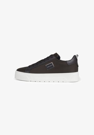 Zapatilla negra de caña baja con parte superior de malla, cordones negros, detalle de piel en el talón, suela blanca gruesa y etiqueta de la marca en el panel lateral.