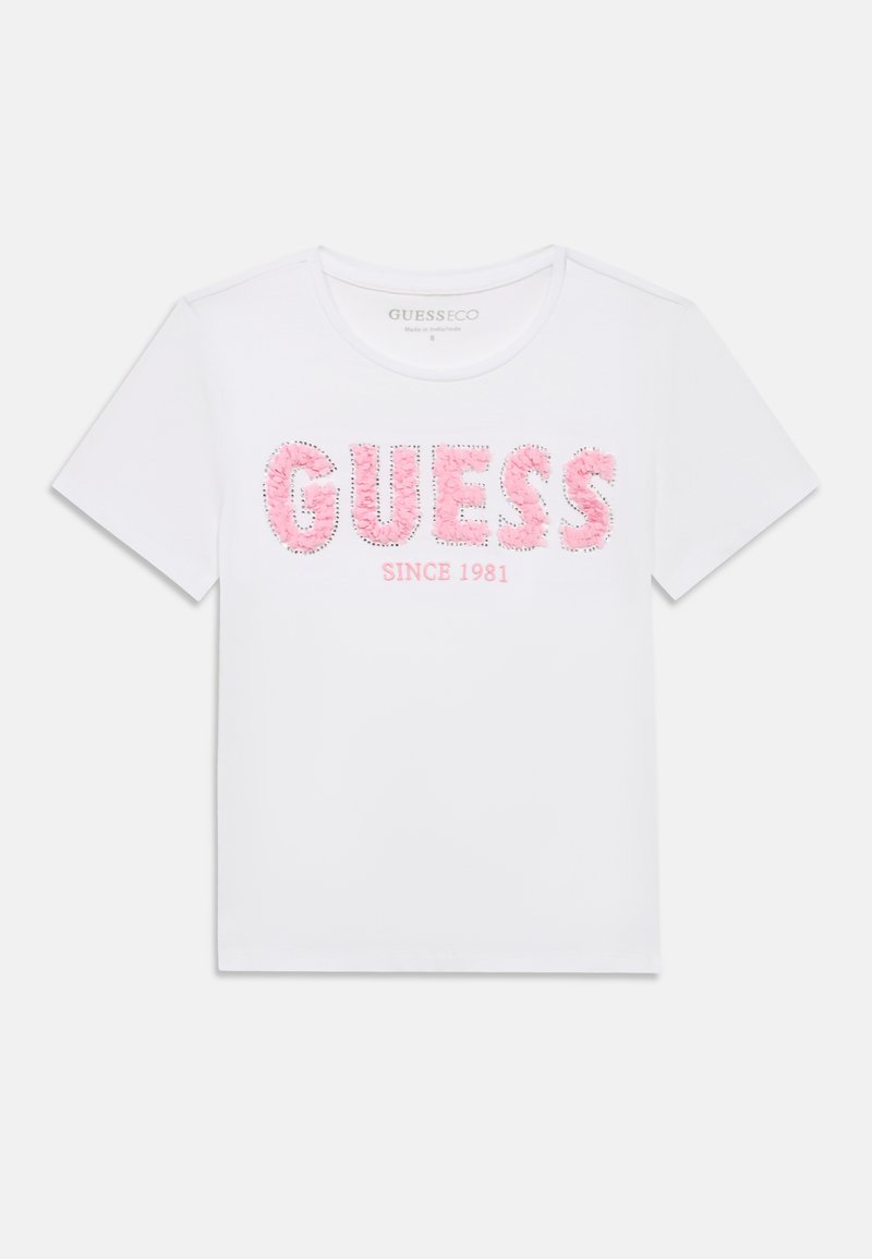 T-shirt blanc à manches courtes avec "GUESS" en lettres florales roses et "SINCE 1981" imprimé en dessous en texte rose.