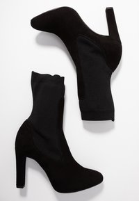 Botas de tacón alto negras con parte superior de ante y detalle de calcetín de punto en el tobillo, con un acabado suave y diseño de punta afilada.