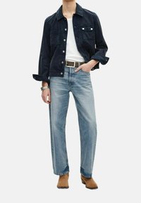 Mörkblå kordjacka med två bröstfickor, vit t-shirt, ljusblå raka jeans och beige ankelstövlar med en silverklocka.