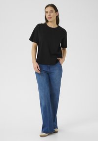 T-shirt nera in cotone a maniche corte, abbinata a jeans blu a gamba larga e scarpe beige. Design semplice, vestibilità comoda, senza motivi visibili.