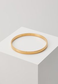 Aukso spalvos metalinė apyrankė, lygi paviršius, apvalios formos, viduje įspaustas tekstas "kate spade - NEW YORK".