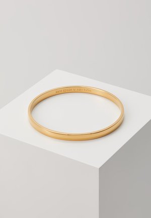 Gold-tone metal bangle bracelet, smooth surface, circular shape, engraved "kate spade - NEW YORK" on the interior.