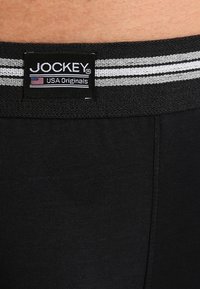 Schwarze Baumwollunterwäsche mit einem weichen elastischen Bund, der zwei graue Streifen hat, und einem schwarzen Etikett mit der Aufschrift "Jockey USA Originals".