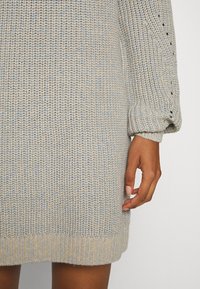 Robe pull tricotée avec une coupe ample, composée d'un mélange de fil bleu clair et beige. Poignets et ourlet côtelés, tissu texturé avec de petits trous.