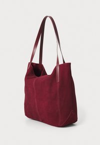 Bordo nubuk torba s dva smeđa kožna držala, koja ima opušteni oblik, glatku teksturu i minimalistički dizajn.