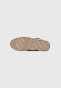 Vue inférieure d'une chaussure avec une semelle en caoutchouc beige, présentant des rainures horizontales et "Calvin Klein" en relief. La partie supérieure est de couleur sombre.