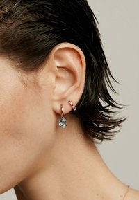 Pendientes de oro rosa con un colgante de gema azul y un aro más pequeño acentuado en rosa. Textura suave con un acabado brillante.
