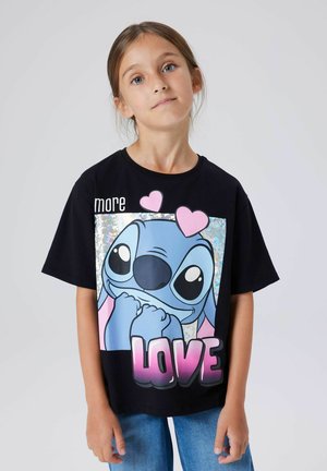 Młoda dziewczyna o jasnobrązowych włosach ubrana w czarny T-shirt z niebieską postacią z kreskówki, sercami i napisem "LOVE" różowymi literami.