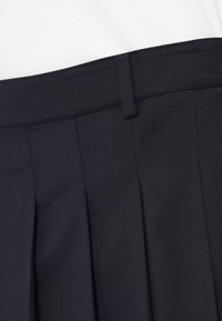 Σκούρες ναυτικές παντελόνες με επίπεδο μπροστινό μέρος, πτυχές και λεία υφή. Η μέση είναι εξοπλισμένη με θηλιά ζώνης.