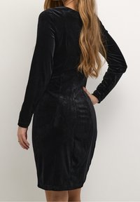 Černé sametové šaty s dlouhým rukávem a přiléhavým střihem, s kulatým výstřihem a hladkou, lesklou texturou.