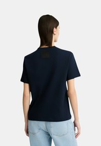 T-shirt in cotone blu navy con maniche corte e un'etichetta quadrata nera sul retro. Abbinato a jeans in denim blu chiaro.