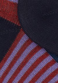 Primo piano di tessuto lavorato a maglia con strisce rosse e viola accanto a sezioni in maglia blu scuro uniforme, che mostrano motivi di punto testurizzati.