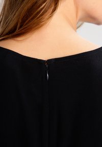 Detalj av en svart klänning som visar rygghalslinjen med en dold dragkedjestängning. Tyget verkar slätt, med en subtil matt finish.