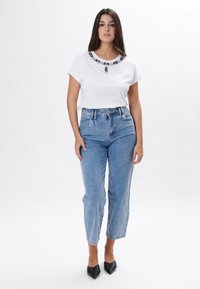 Camiseta blanca de manga corta con un elegante escote decorado con cuentas, combinada con unos jeans de mezclilla claros de tiro alto y tacones negros de punta.}}