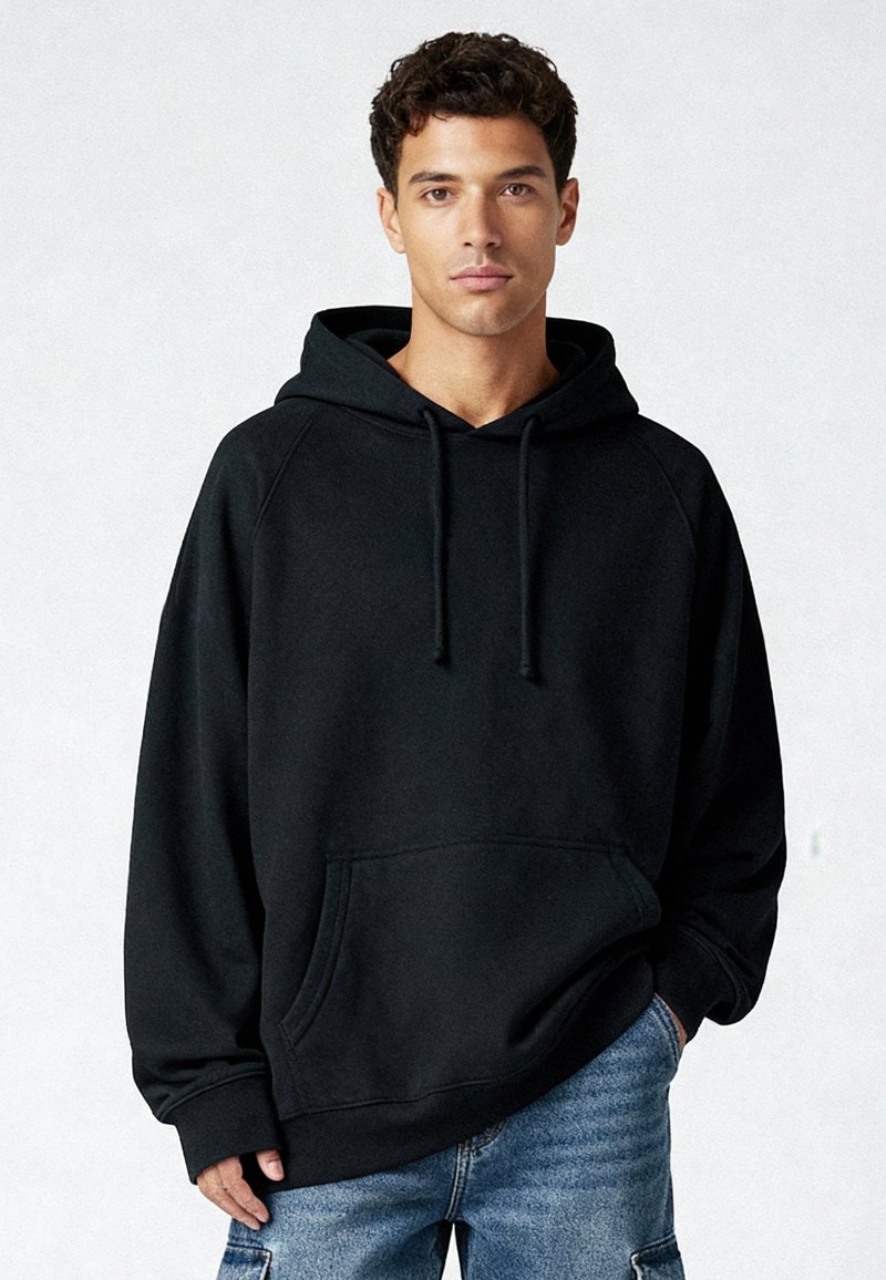 Zwarte oversized hoodie met een koord, een kangaroozak aan de voorkant en geribbelde manchetten, gedragen met lichtblauwe denim shorts. Gladde textuur.