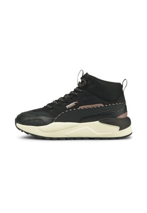 Baskets mid-top Puma noires avec semelle blanche, semelle extérieure texturée antidérapante, lacets noirs à motifs et petit accent métallique marron près du talon.