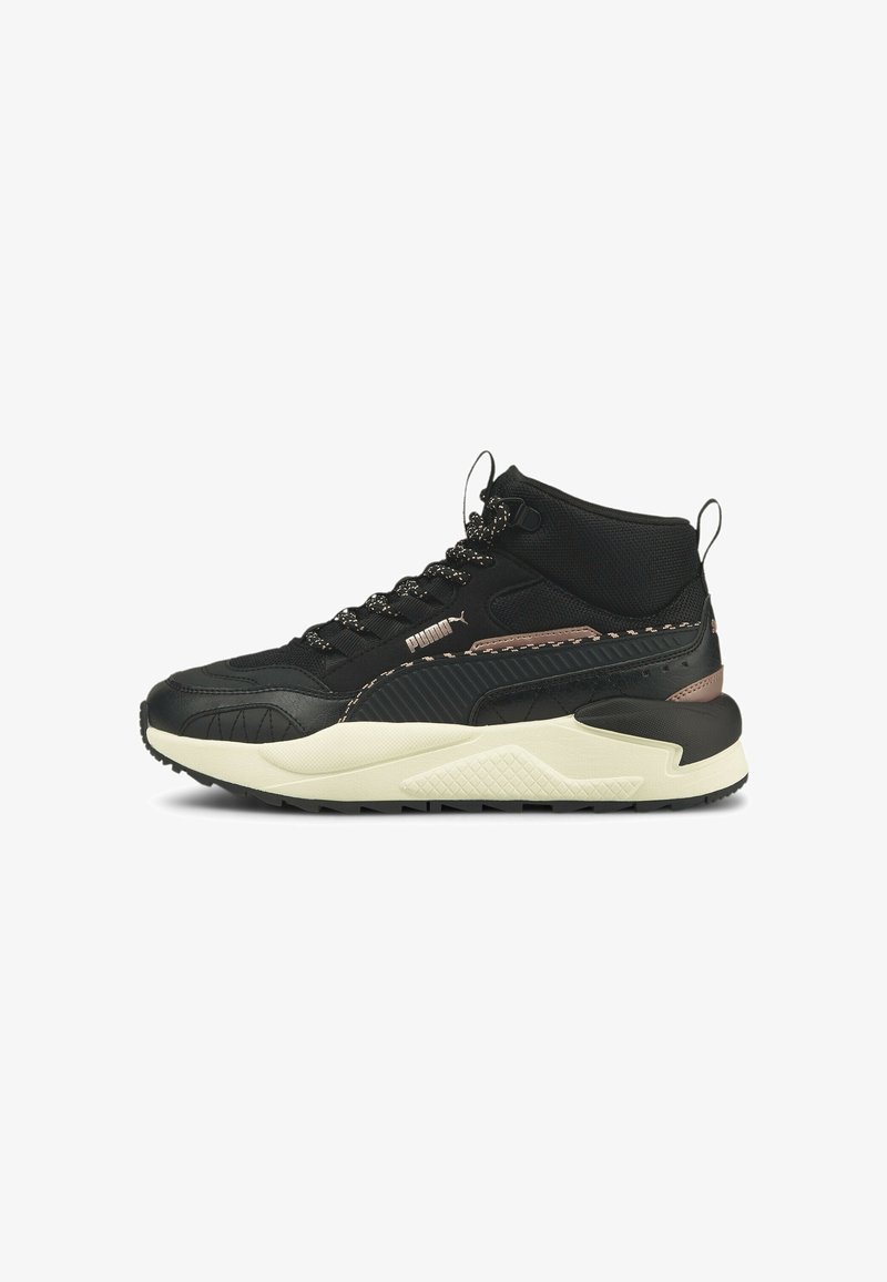 Baskets mid-top Puma noires avec semelle blanche, semelle extérieure texturée antidérapante, lacets noirs à motifs et petit accent métallique marron près du talon.
