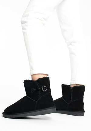 Schwarze Wildleder-Ankle Boots mit runder Zehenform, weichem Innenfutter und dekorativem Knopfdetail an der Seite. Gummisohle für guten Grip.