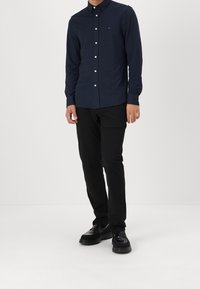 Camisa azul marino con botones y un patrón sutil, con cuello y botones blancos, combinada con pantalones negros y zapatos negros.