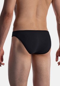 Black swim briefs with a smooth texture and low-rise design, featuring a stretchy waistband and seamless sides, worn on a bare torso.