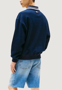 Felpa blu navy con colletto a righe bianche, vestibilità comoda e polsini a costine. Abbinata a pantaloncini di jeans azzurri.