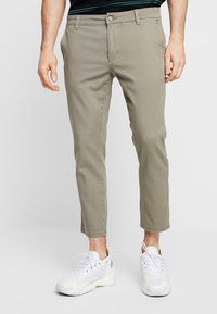 Cropped chino verde chiaro in cotone, con chiusura a bottone e cerniera, tasche frontali e una texture liscia. Indossati con sneakers bianche.