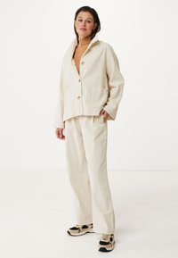 Krémová kordověná bunda s šálovým límcem a knoflíky, spárovaná s odpovídajícími širokými kalhotami. Černé a hnědé tenisky s detaily.