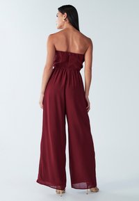 Burgundski brez naramnic kombinezon z nabranim zgornjim delom in širokimi hlačnicami, iz lahkega blaga, z glatko teksturo.