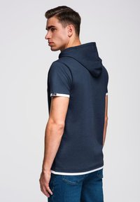 Námořnická modrá mikina s kapucí a krátkými rukávy s bílým lemem. Měkká tkanina, přiléhavý střih, jednoduchý design a detail vrstveného spodního lemu.